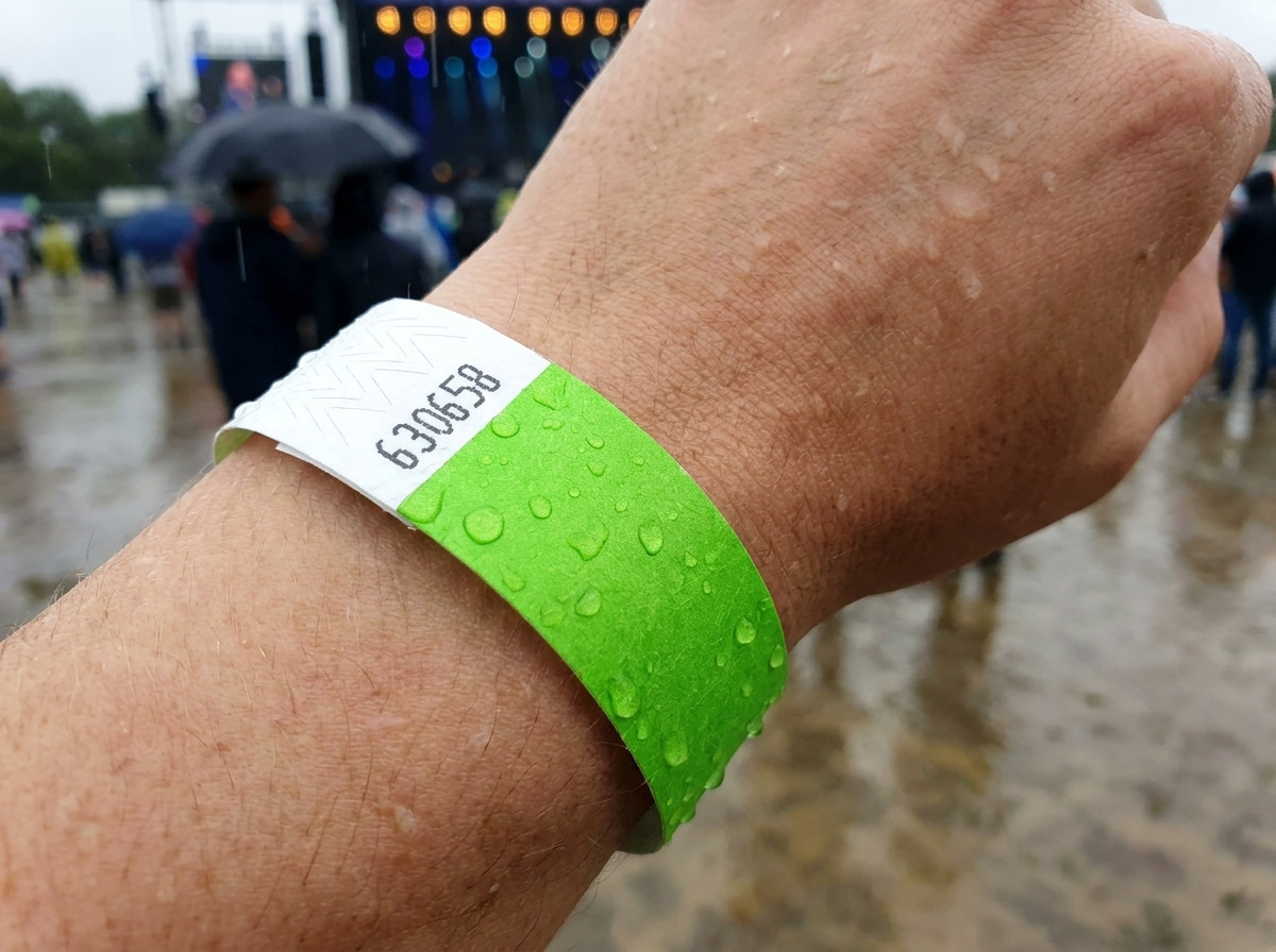 pulsera identificativa llevada en la muneca bajo la lluvia durante un festival al aire libre, ilustrando su resistencia al agua y a la humedad
