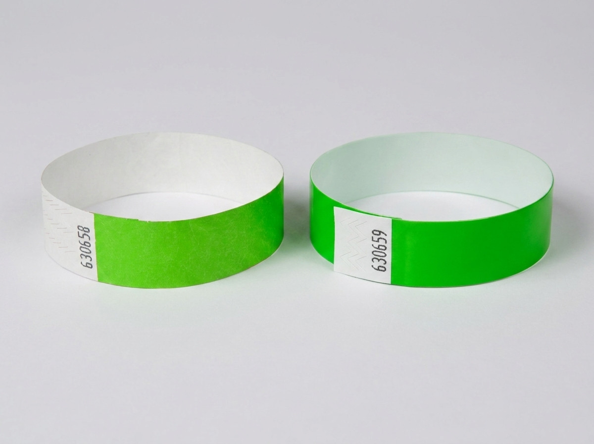 Comparacion en paralelo de una pulsera Tyvek blanca con codigo de barras impreso y una pulsera identificativa de color con codigo de barras, colocadas sobre una mesa de festival