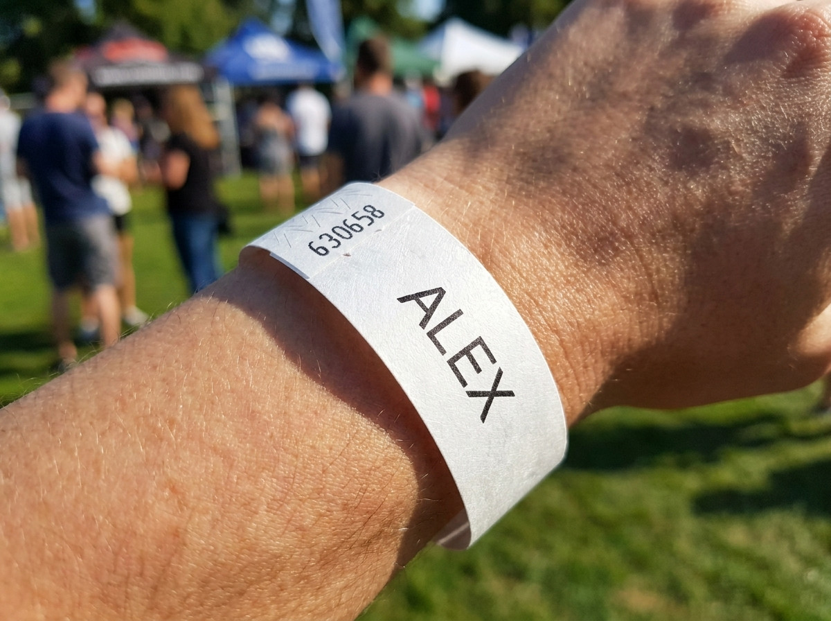 Pulsera Tyvek blanca impresa con el nombre de un niño y un número de teléfono de emergencia, llevada en la muñeca de un niño pequeño durante un evento al aire libre